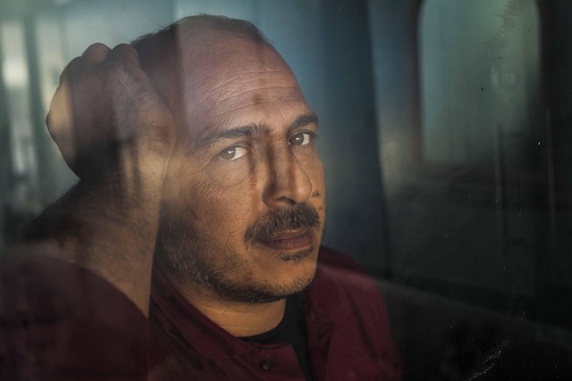 A man looks through a window with one hand resting on his head.